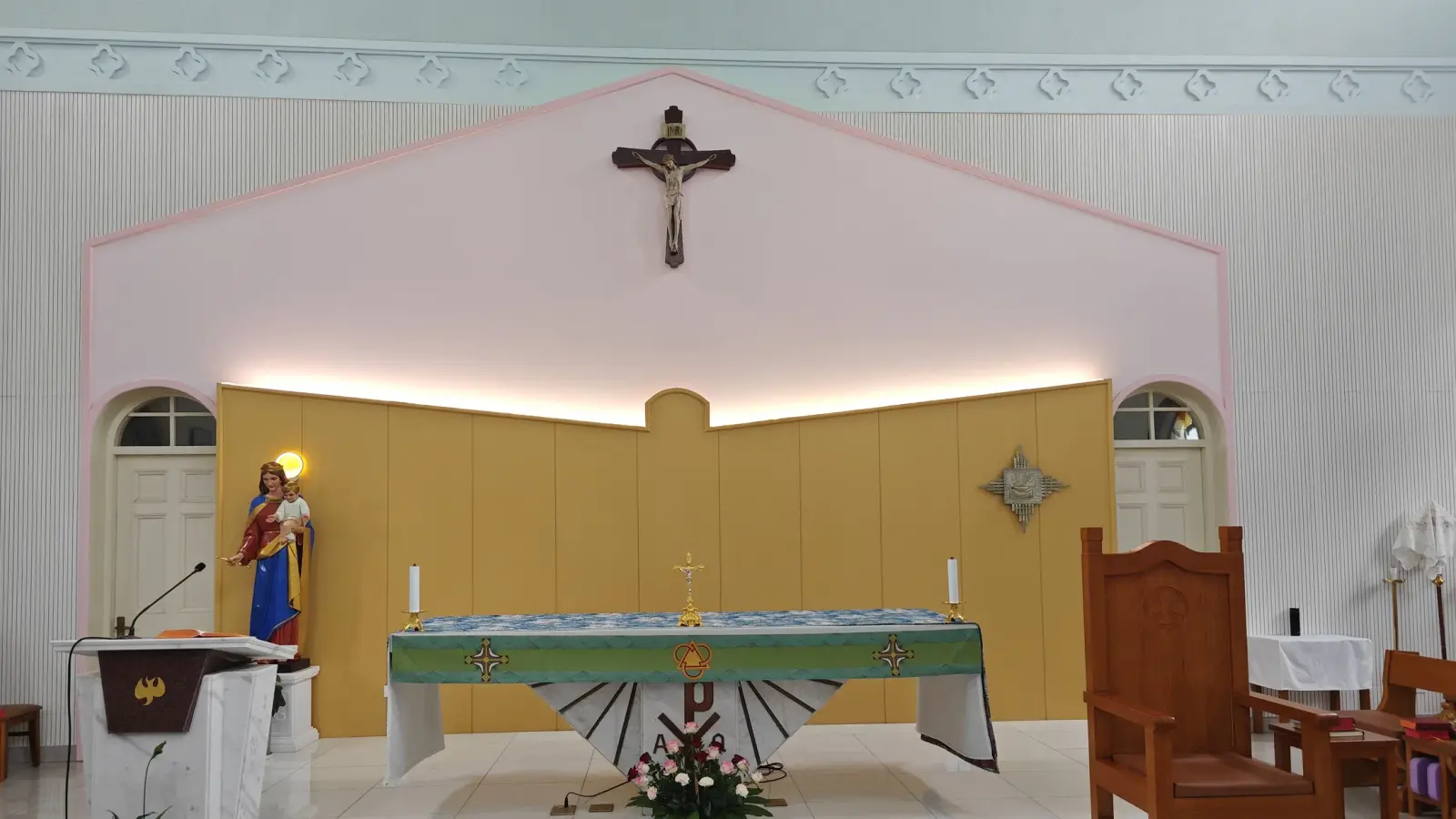 A pink arched recess with a crucifix above an altar covered with a green cloth and a statue on the left.