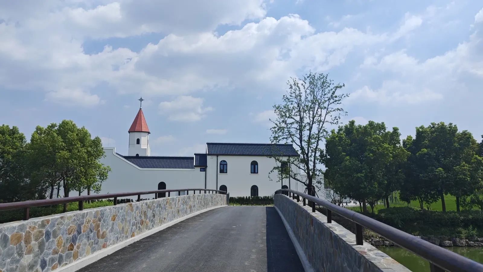 A paved bridge with stone parapets leading to white buildings and a small tower with a red roof.