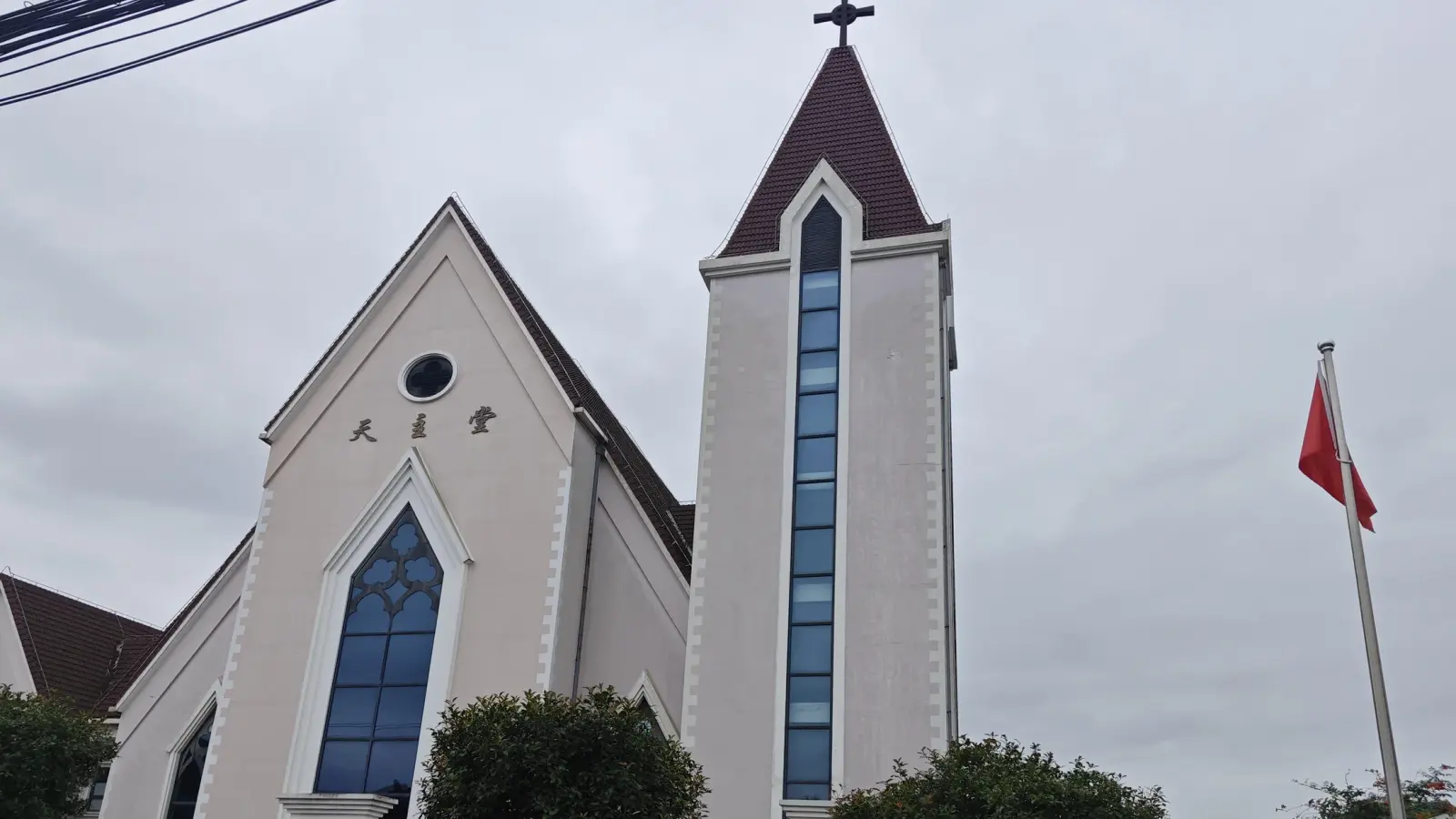 A narrow tower with a dark pointed roof and a tall blue window beside a gable with a round window, under a grey sky.