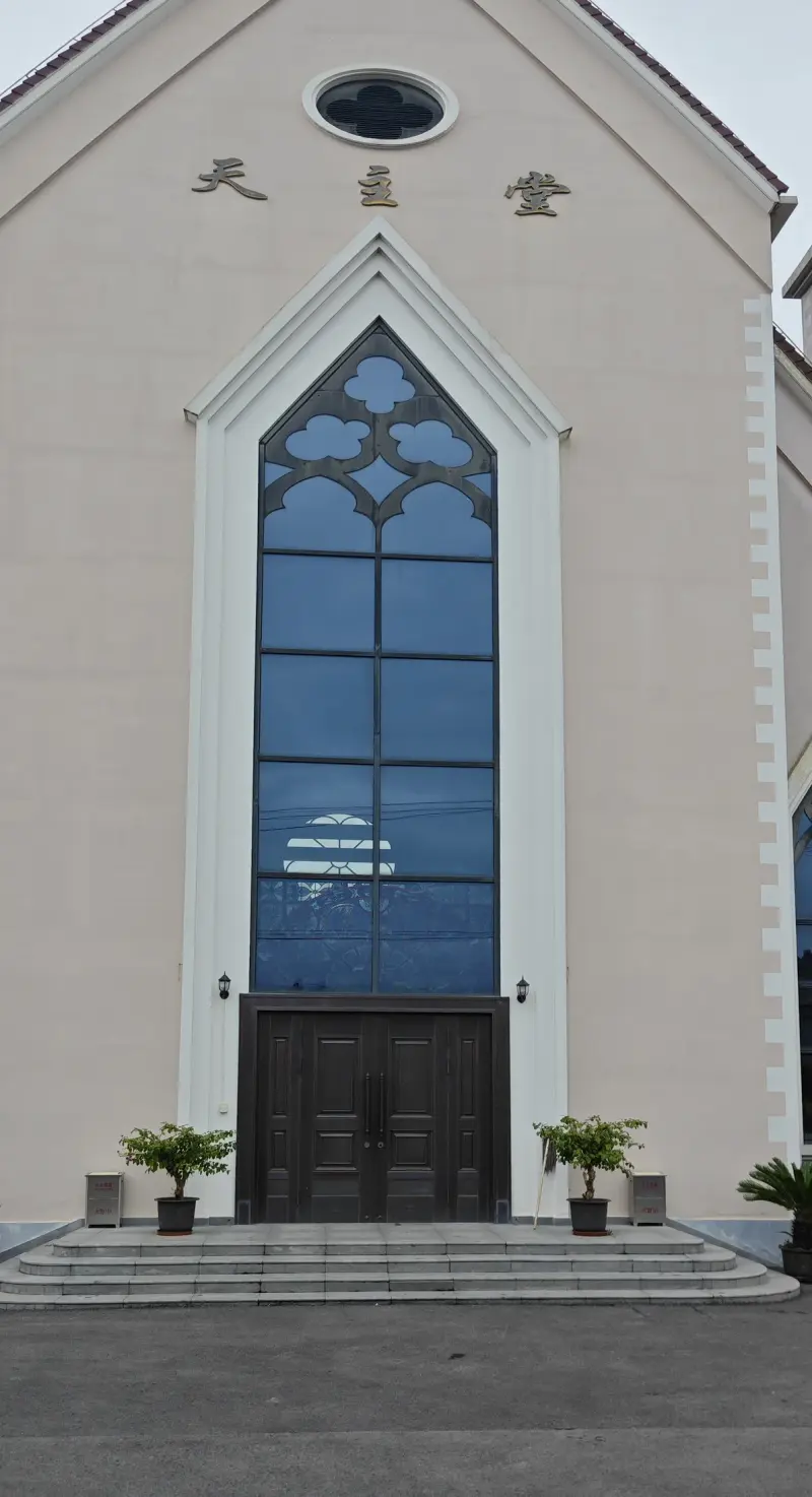 A cream gable front with a tall pointed blue window, an oval window above, and brown double doors at the foot of low steps.