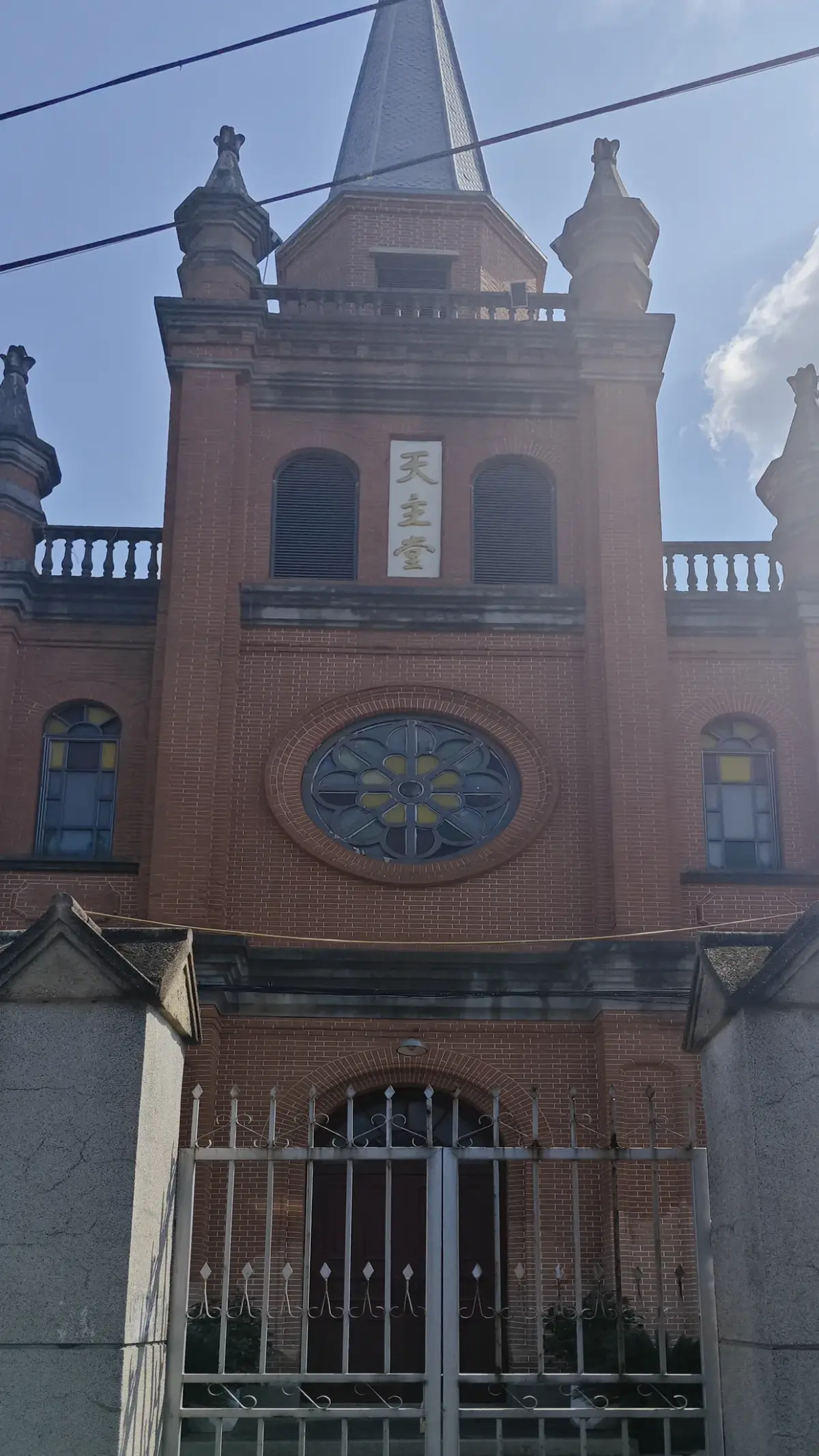 An orange-brick tower with turrets, a round window and a pointed spire seen from below.