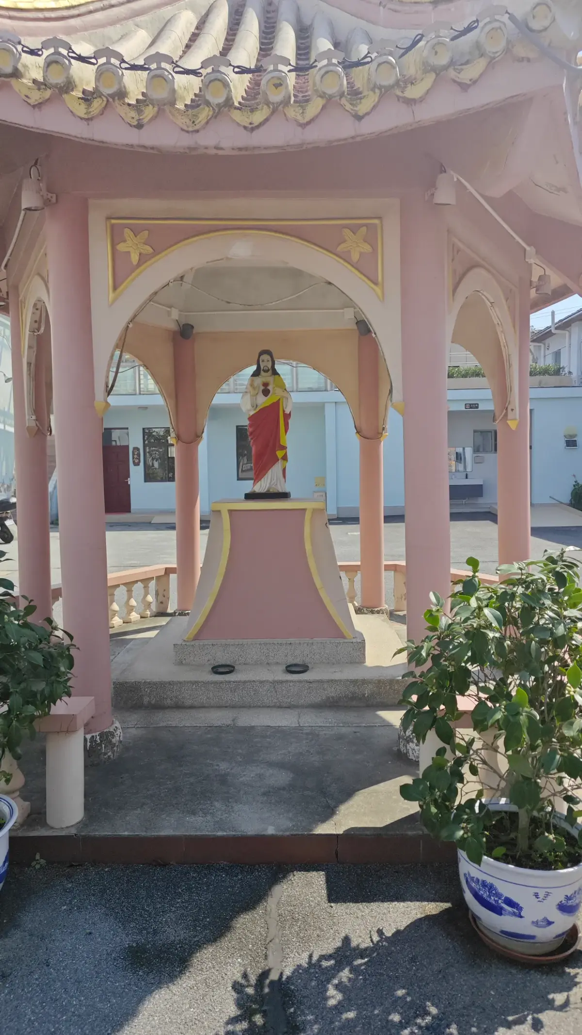 A pink open pavilion with a decorated roof and a statue of Christ on a pedestal.