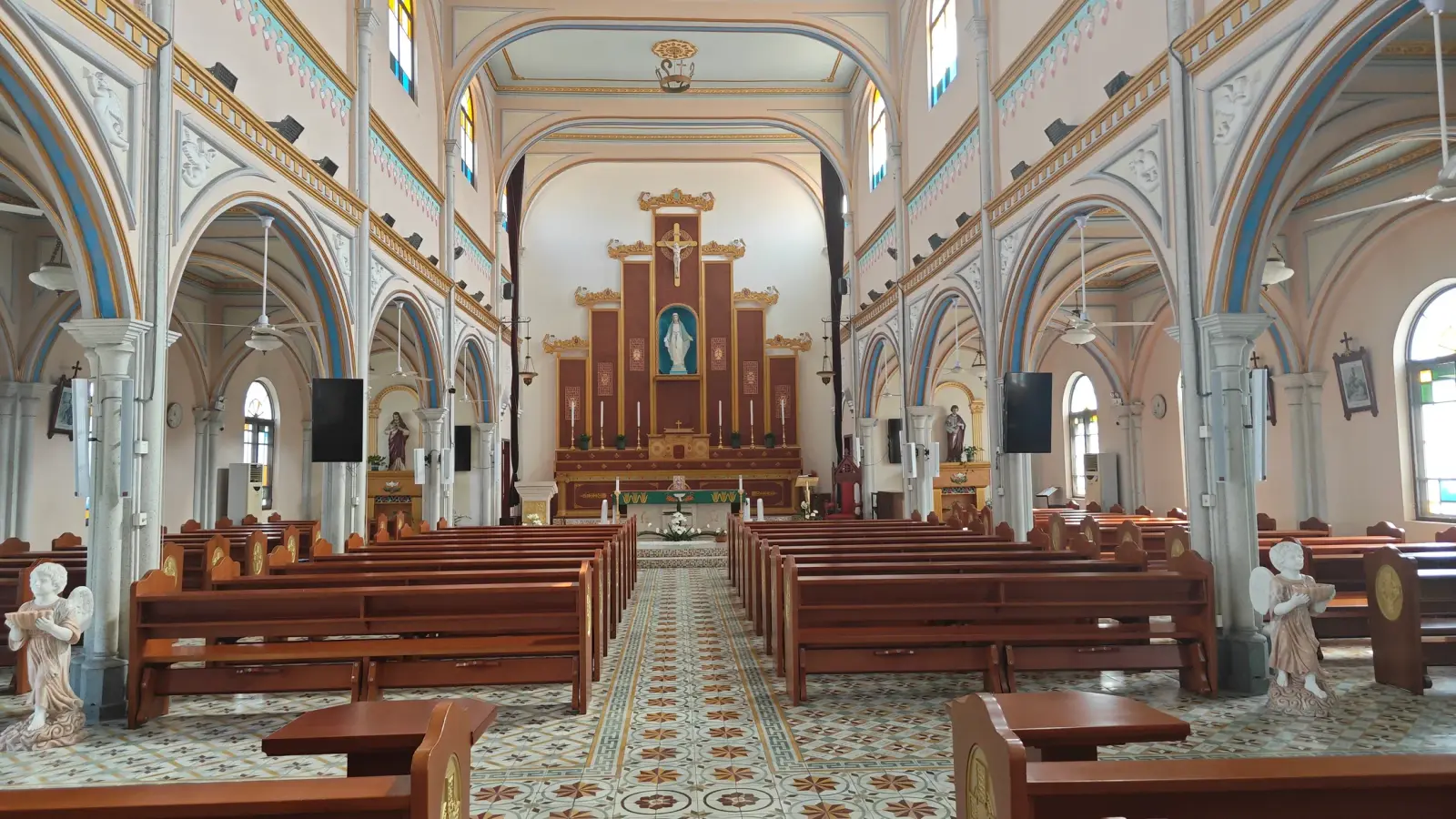 A church interior with pale arches in blue and gold, a patterned tile aisle and a decorated altar.