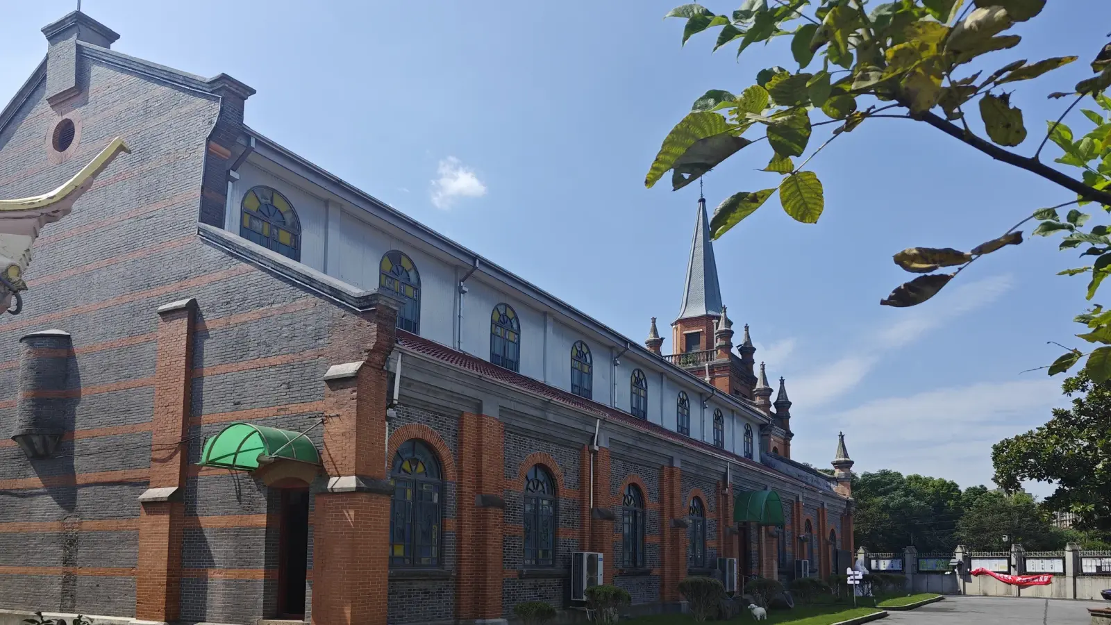 A banded brick church side wall with arched windows, a green canopy over a door and a spire at the end.