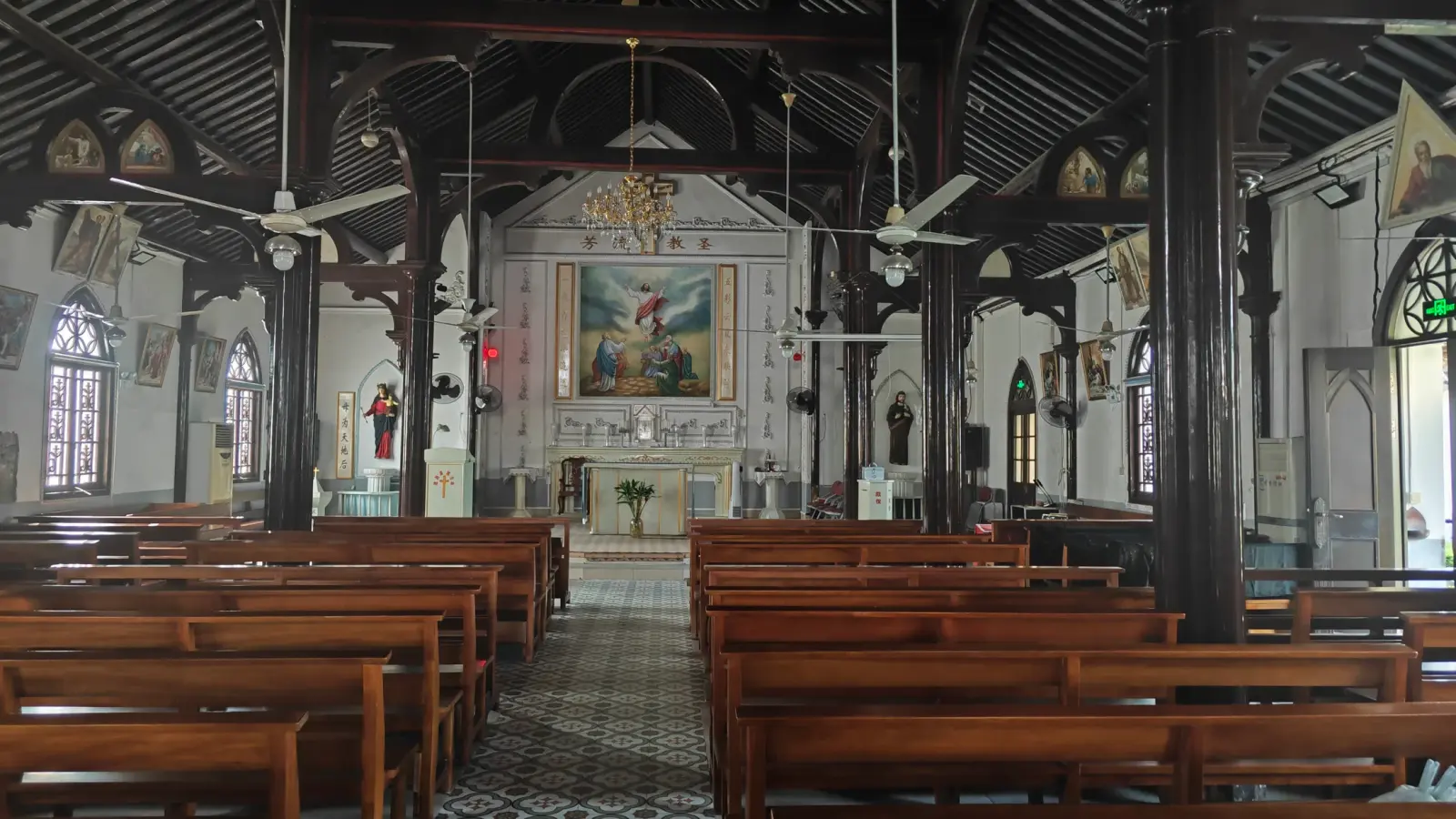 The church interior with black wooden pillars, wooden benches and a painted altar at the far end.