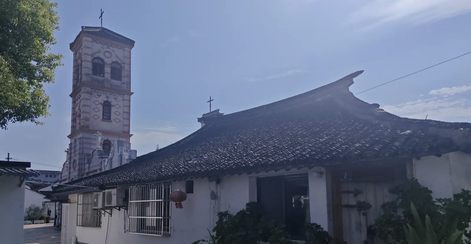 A brick bell tower behind a traditional curved tiled roof under a blue sky.