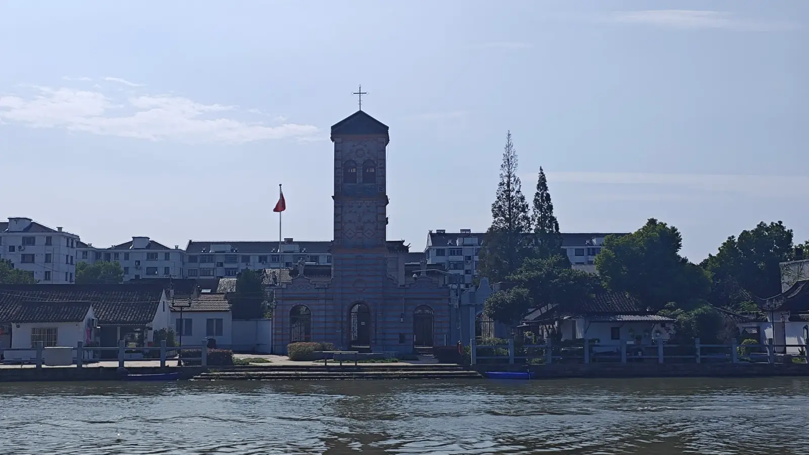 A square church tower rising above low buildings across a stretch of canal water.