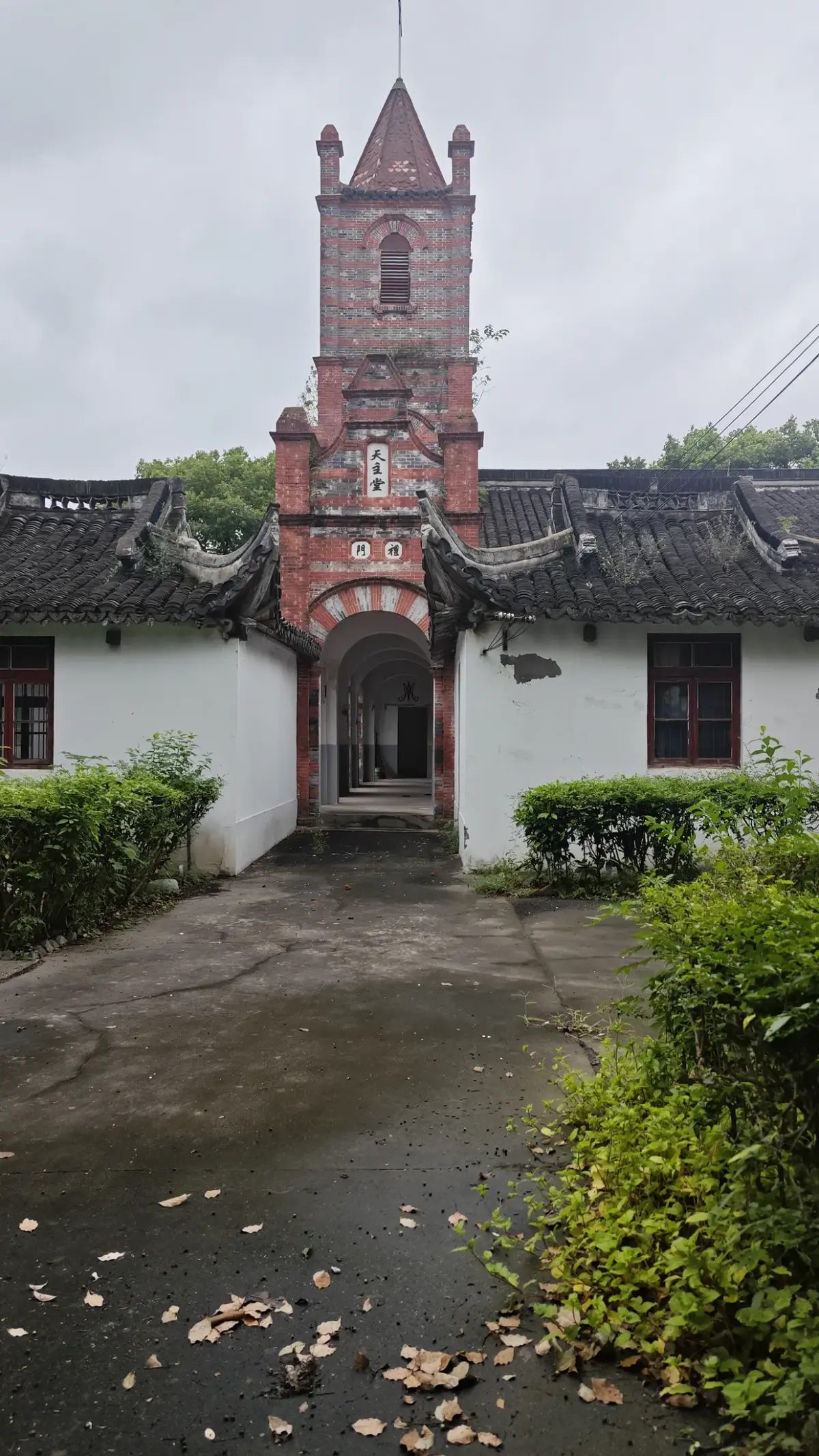 A red brick tower with a pointed roof above a white-walled, tile-roofed gatehouse at the end of a path.