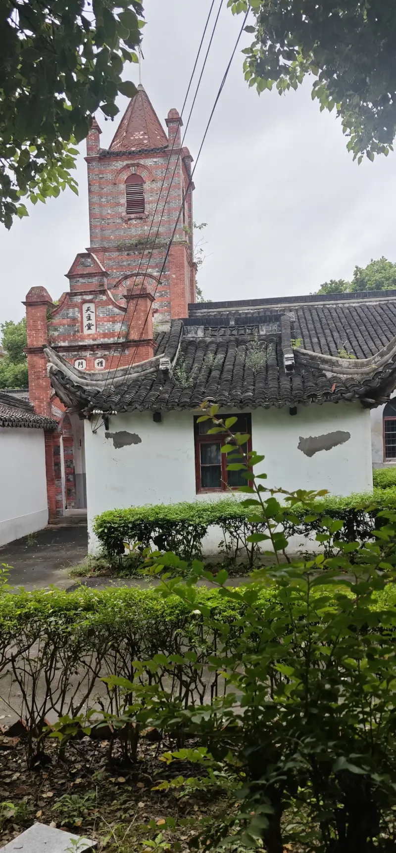 A red brick tower behind a traditional tiled roof and clipped hedges.