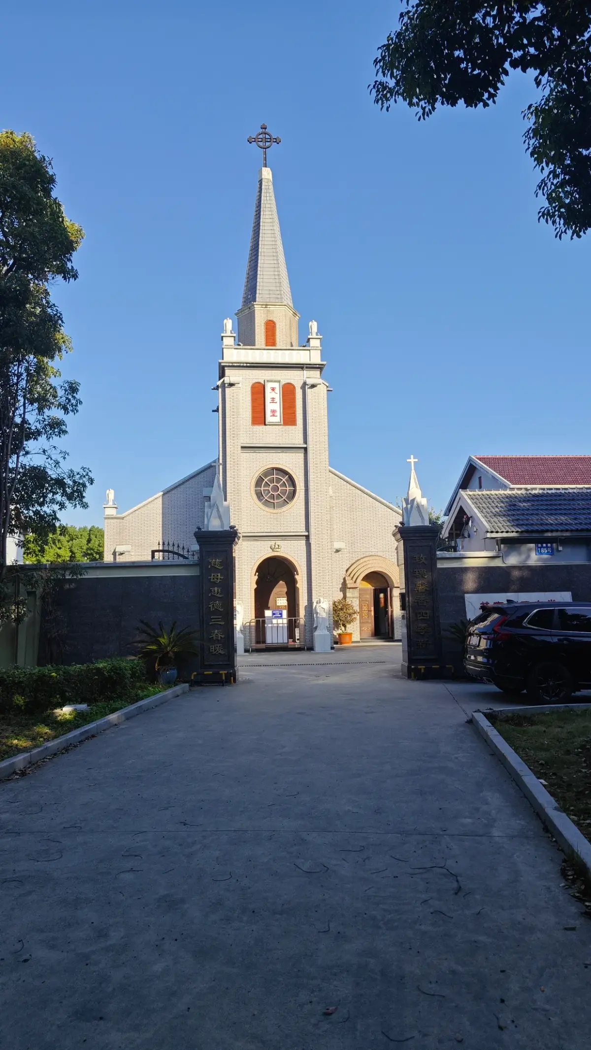 A pale church with a thin spire at the end of a stone-paved lane between trees.