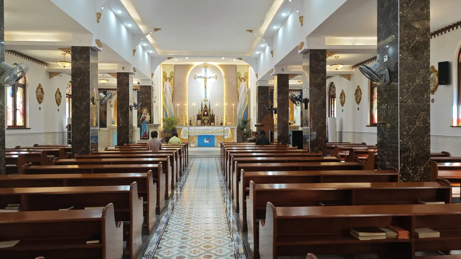 A church interior with brown wooden pews, dark columns and a crucifix at the far end.