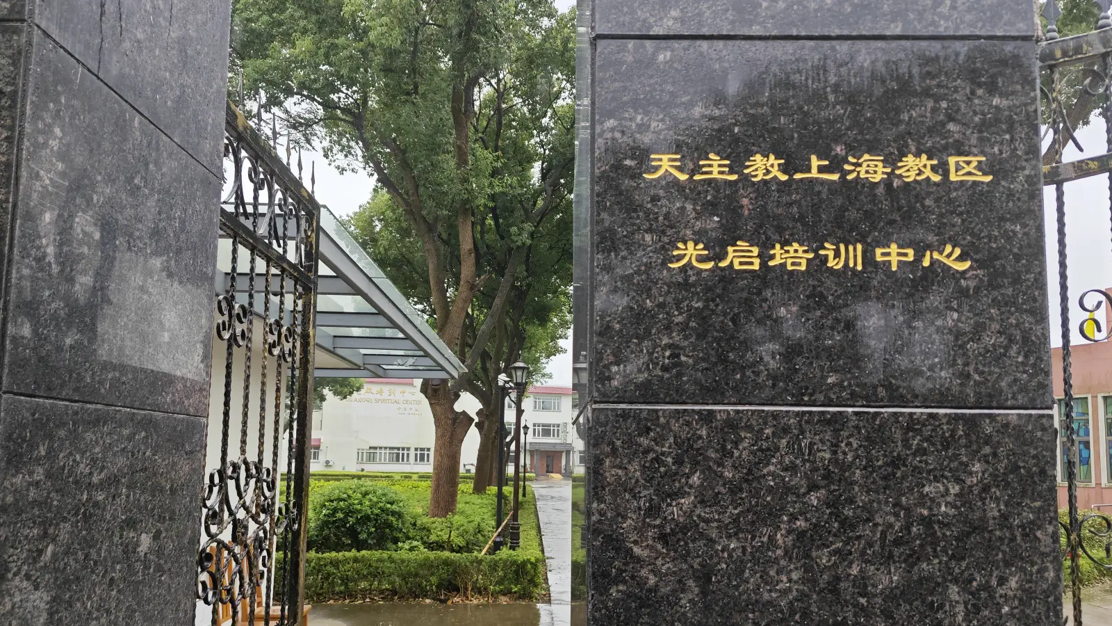 A polished black granite gatepost with gold Chinese characters, beside an open iron gate.