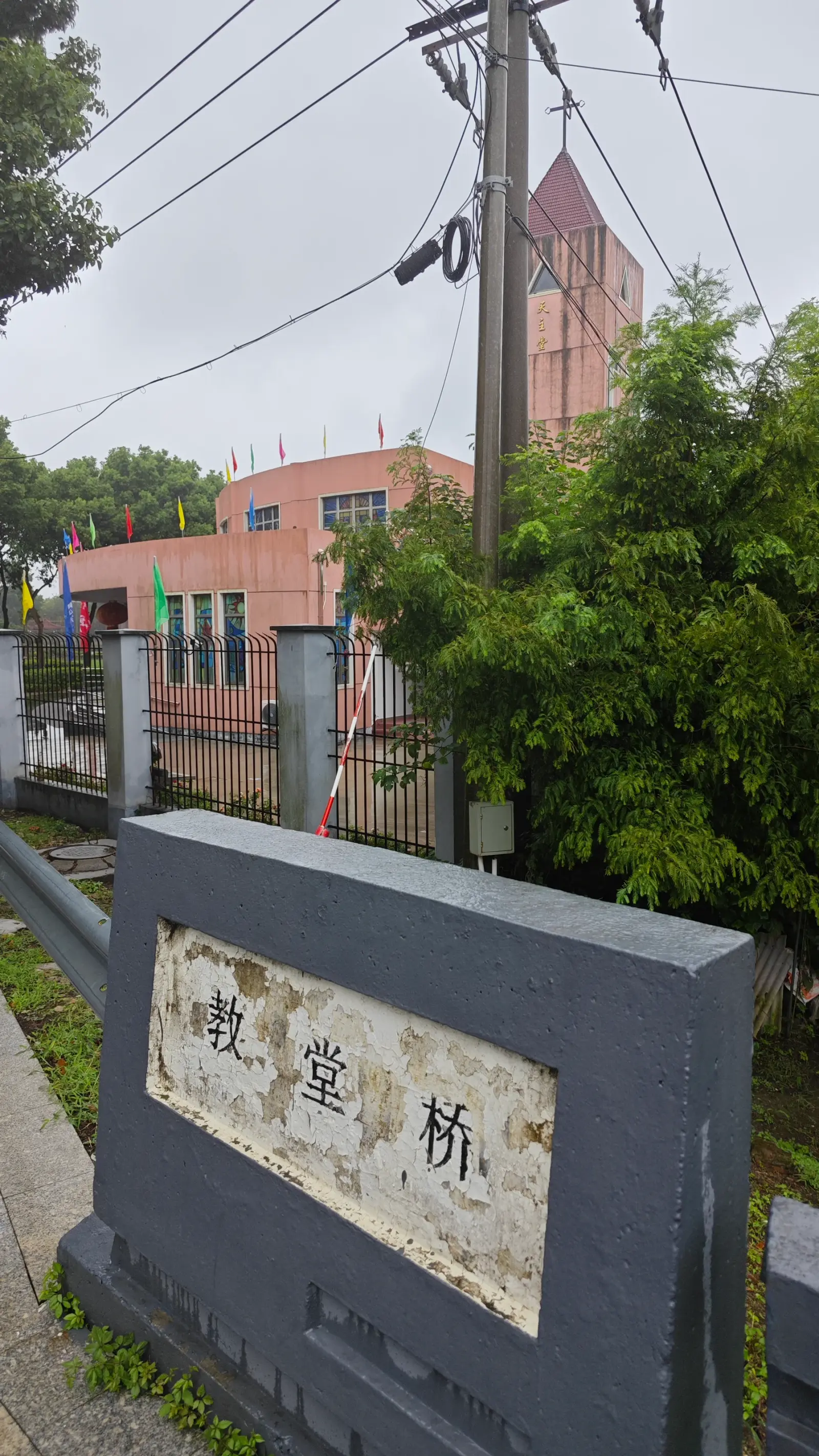 A grey stone block bearing white Chinese characters at a roadside, with a pink tower behind trees and wires.