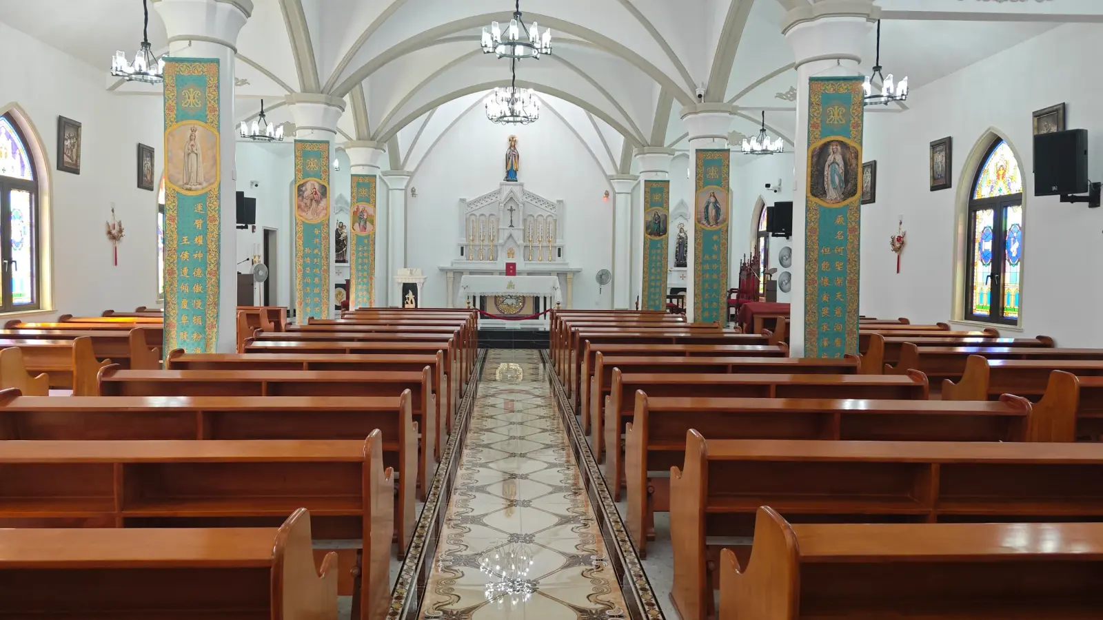 A church interior with a white vaulted ceiling, green painted columns, wooden pews and a patterned tile aisle.