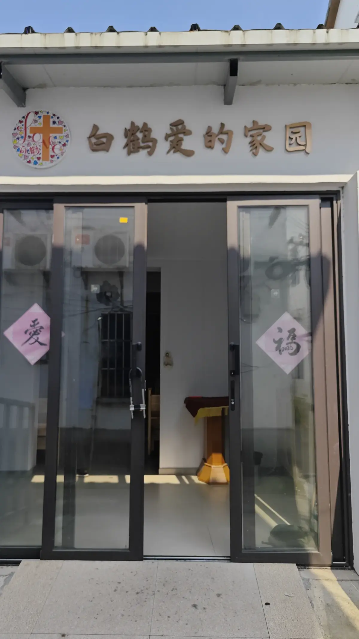 A glass door entrance under a grey sign with a cross emblem and Chinese characters, with paper decorations on the glass.