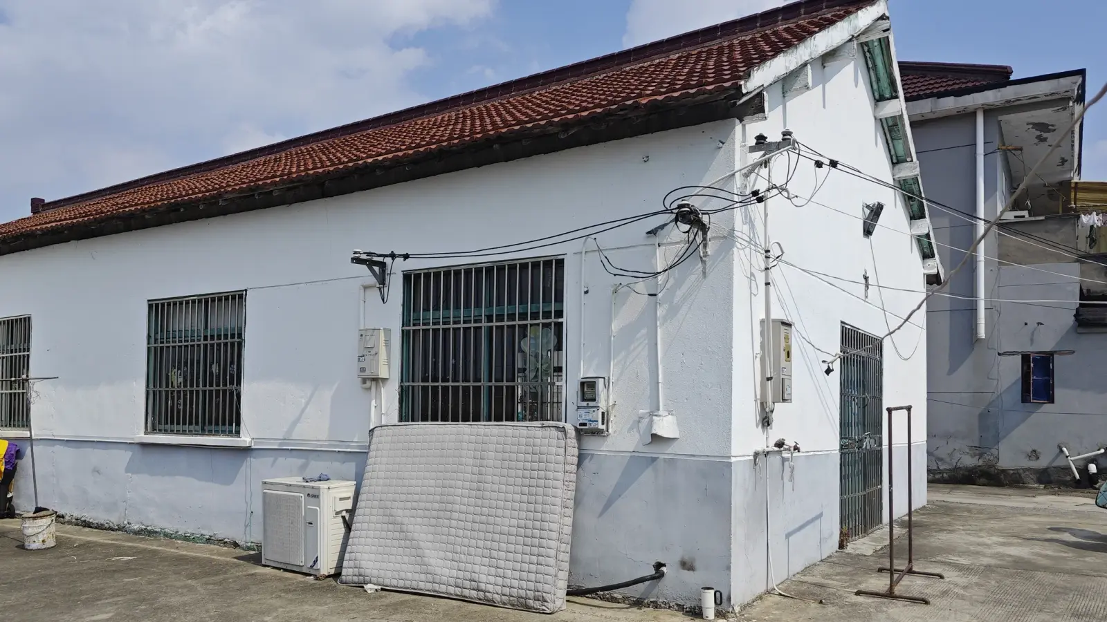 A white building with a long red tile roof, barred windows and a concrete yard.