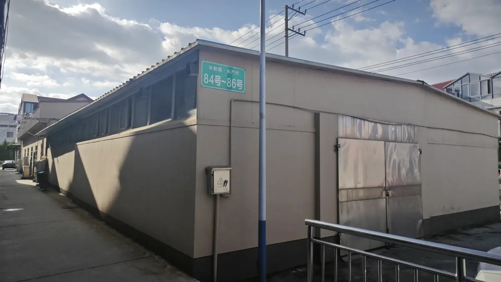 A beige single-storey building with a long sloped roof and a green address sign on its wall.