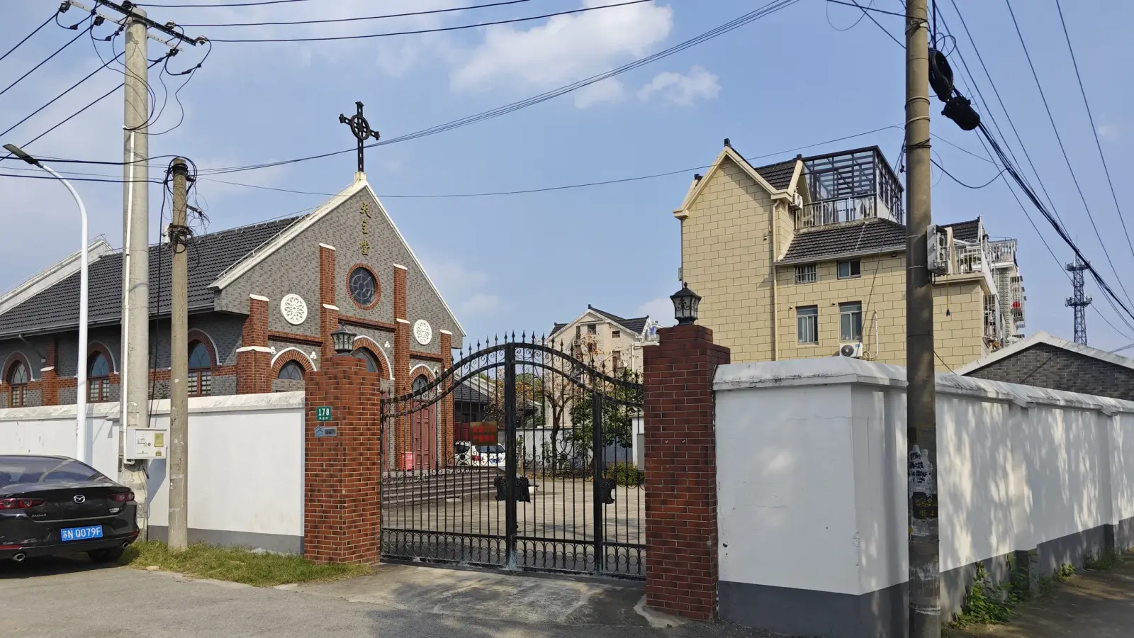 A grey and red brick church behind a brick-pillared iron gate, with a modern apartment block beside it.
