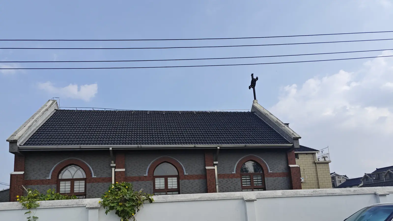 A dark-tiled church roof and a grey brick side wall with arched windows and a cross on the gable.