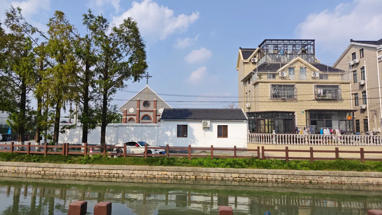 A small gabled church front beside white buildings and modern houses, across a stretch of canal.