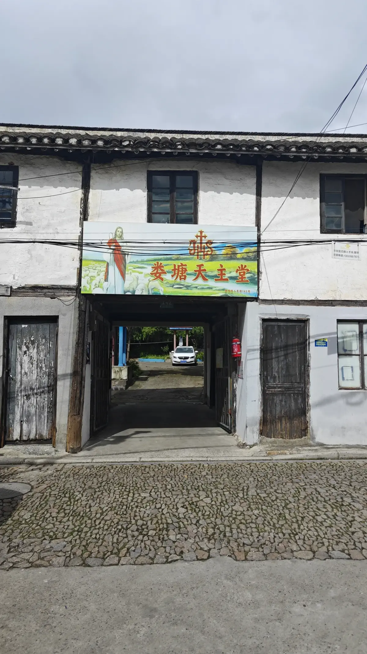 A weathered two-storey white building with an open passage and a painted banner sign above it, on a cobbled forecourt.