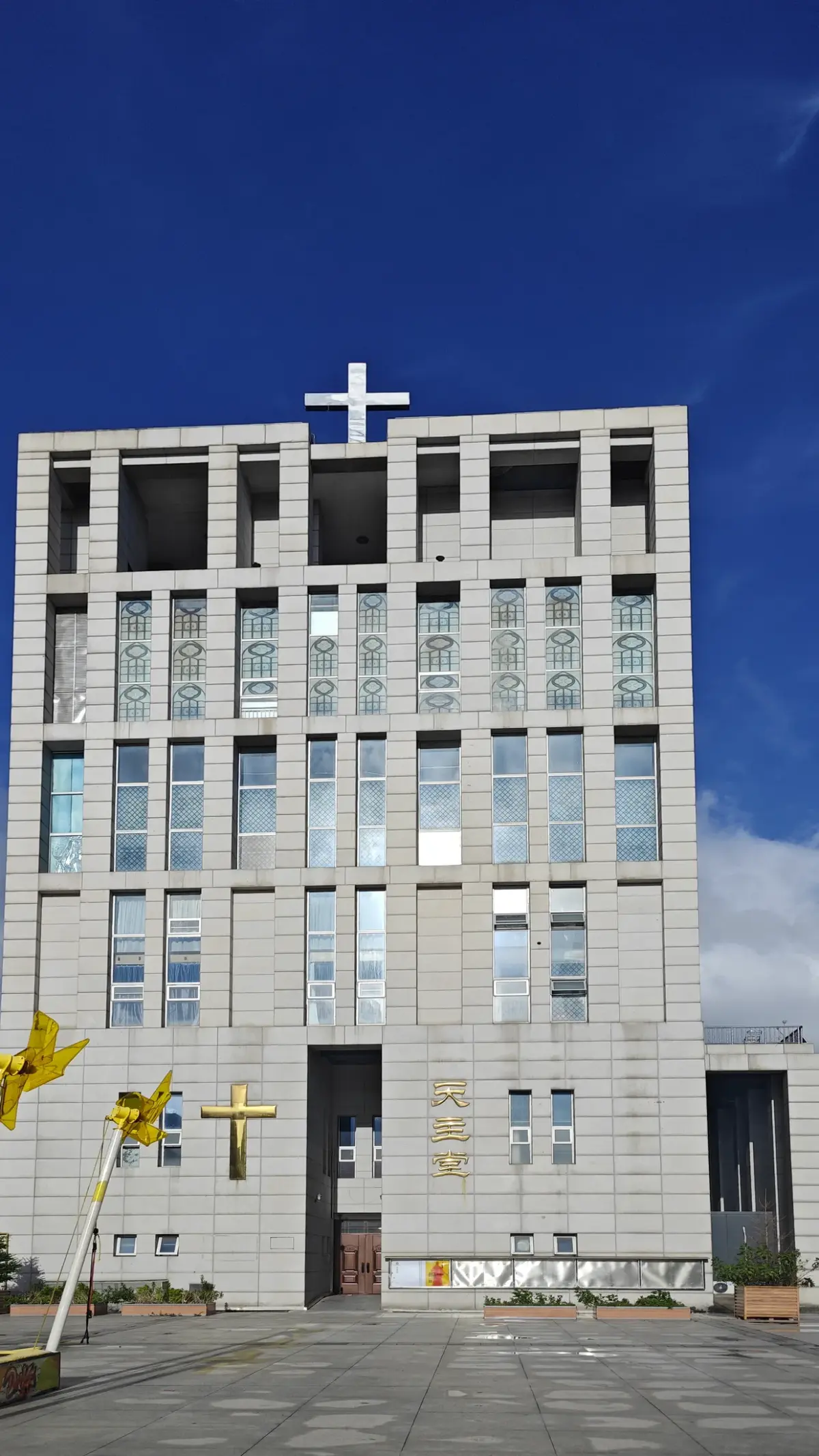 A grey stone tower with rows of narrow windows and a cross at the top against a deep blue sky.
