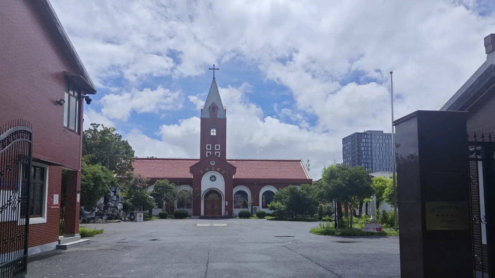 A red-roofed church with a central tower at the far end of a paved courtyard behind iron gates.