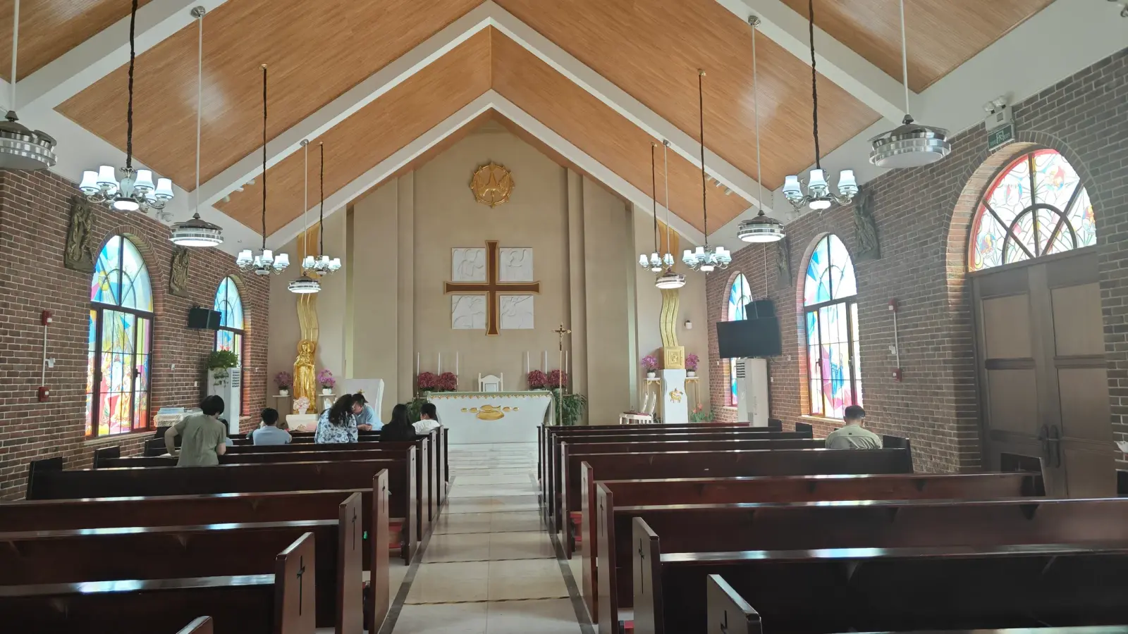 A church interior with exposed brick walls, a pitched timber ceiling, dark wooden pews and stained glass windows.