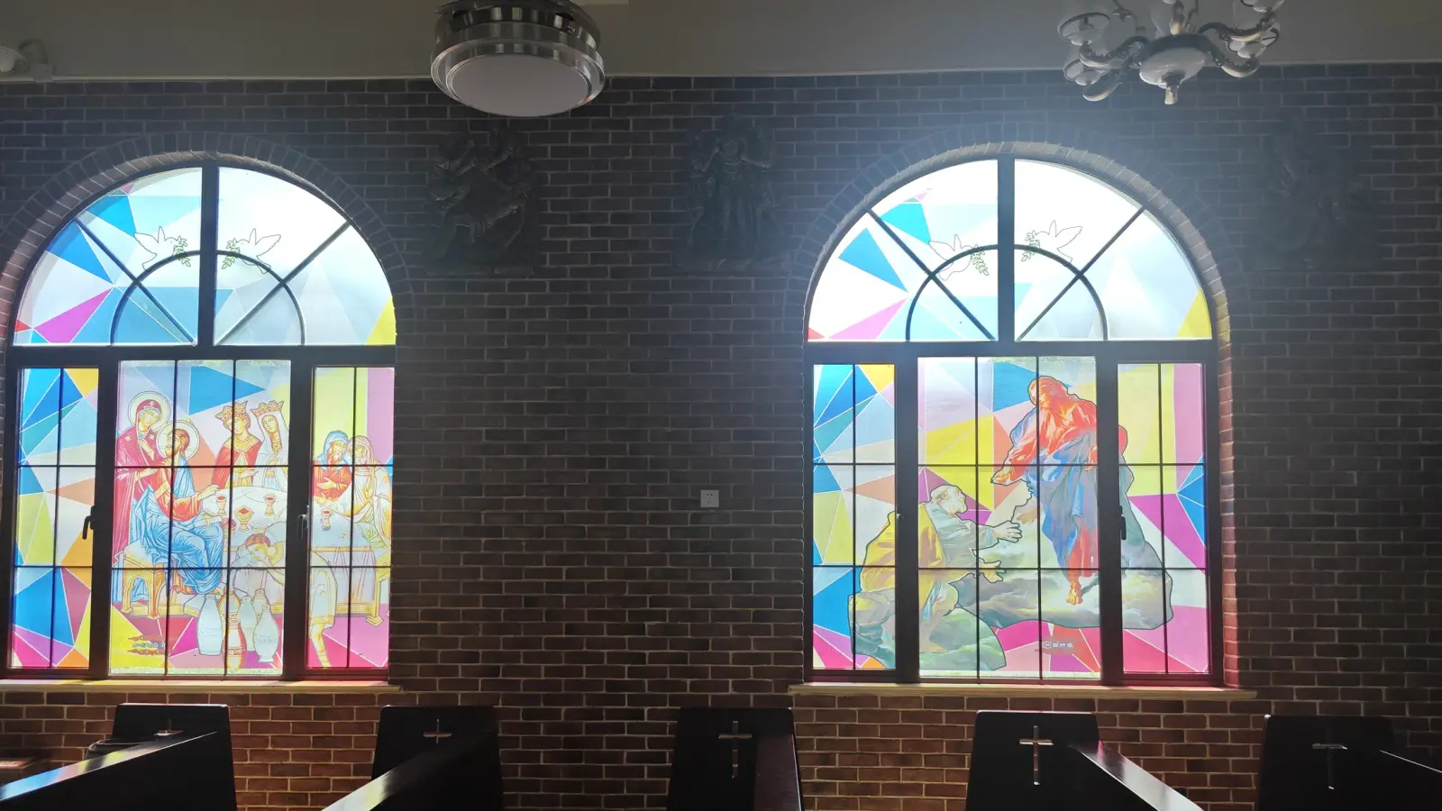 Two tall arched windows of bright pink, yellow and blue glass depicting religious figures.