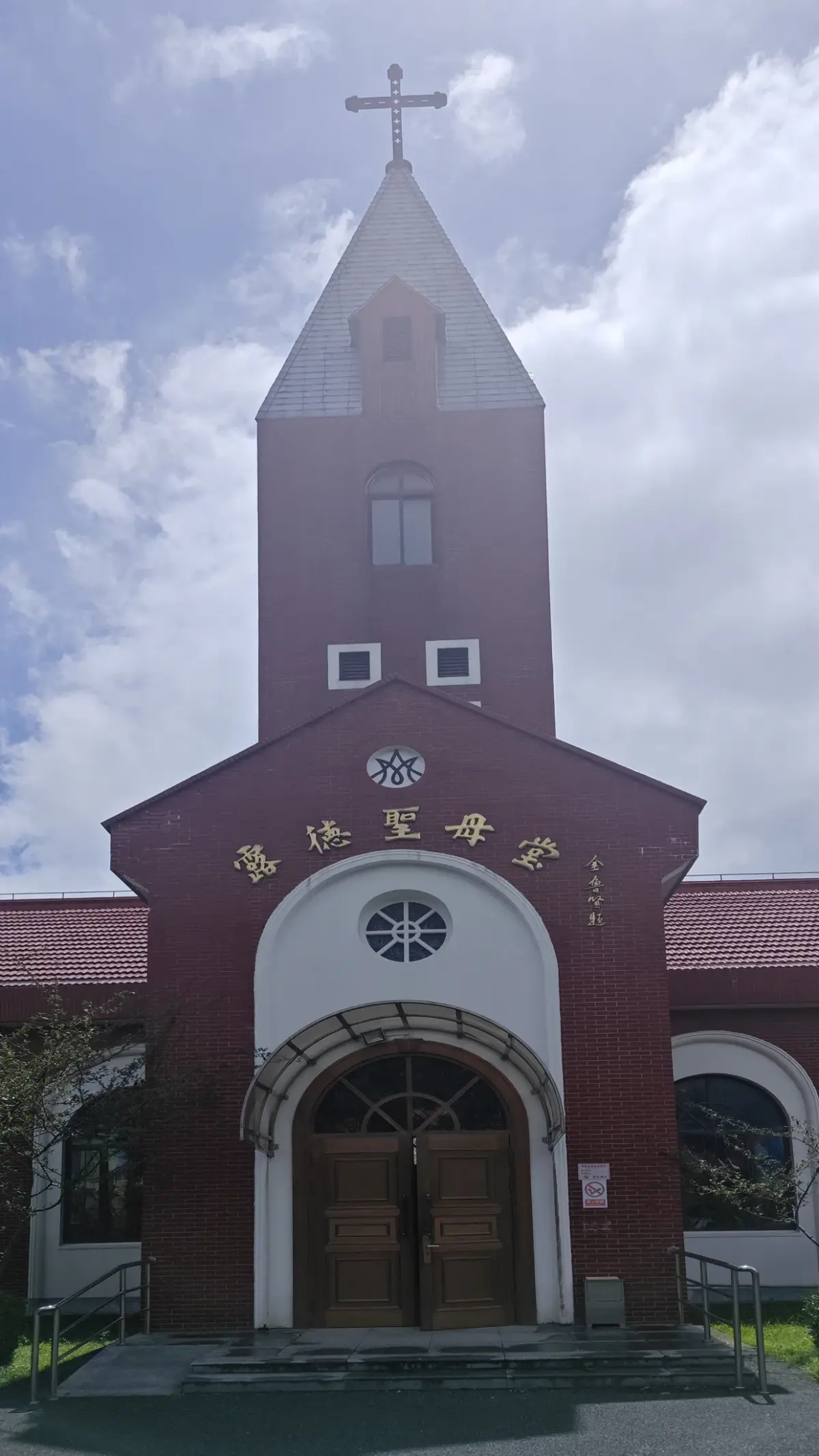 A red-brick tower with a pointed grey spire and cross above an arched wooden doorway.