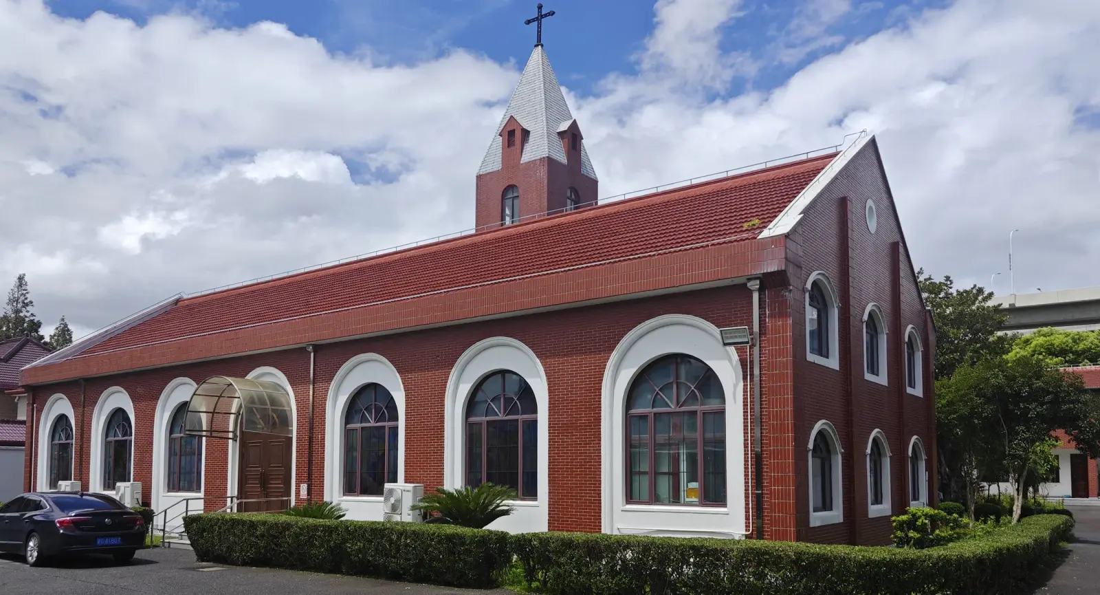 A red-brick church with white-framed arched windows, a gable end and a slender white spire under a blue sky with clouds.