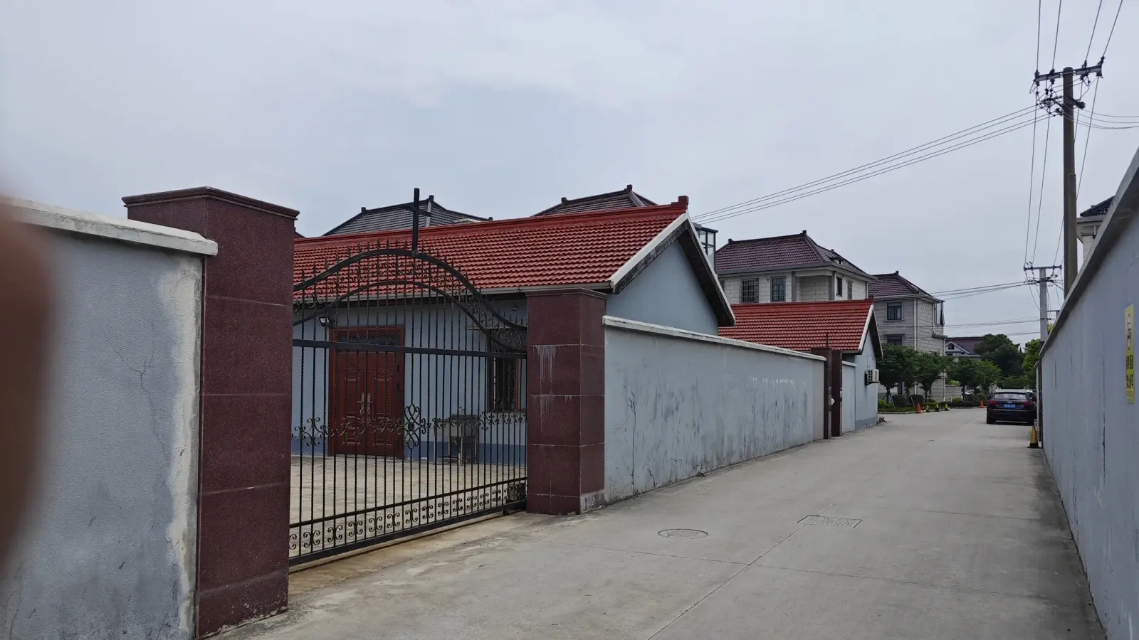 A narrow concrete lane running past a red-tiled blue building behind a maroon and grey gate.