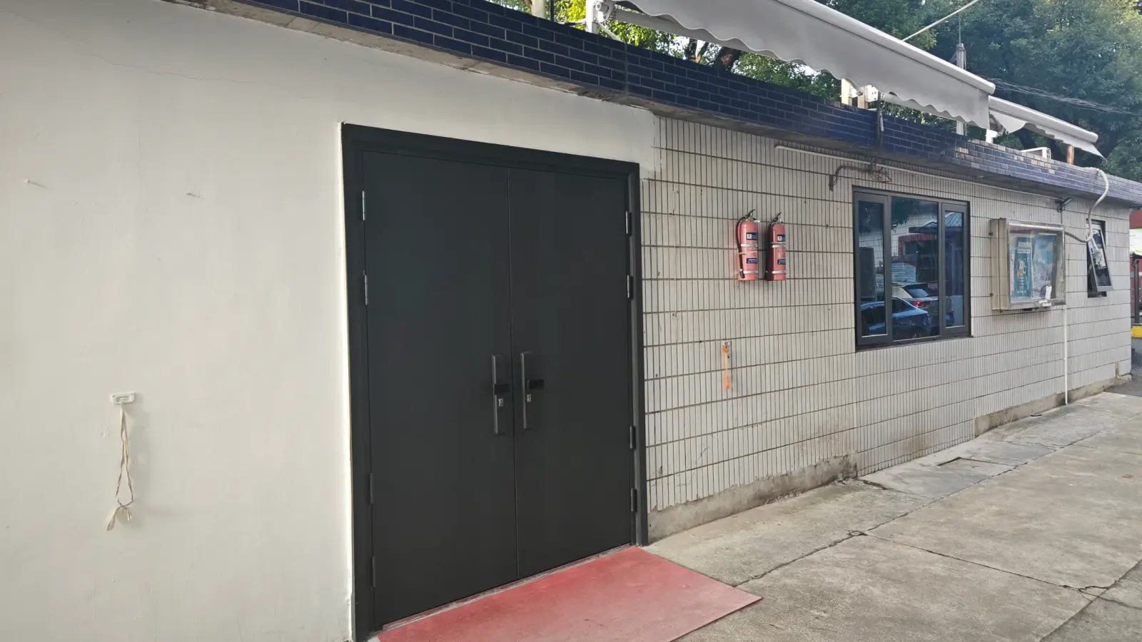 A low white building with a tiled lower wall, a dark double door and a window under a blue-tiled eave.