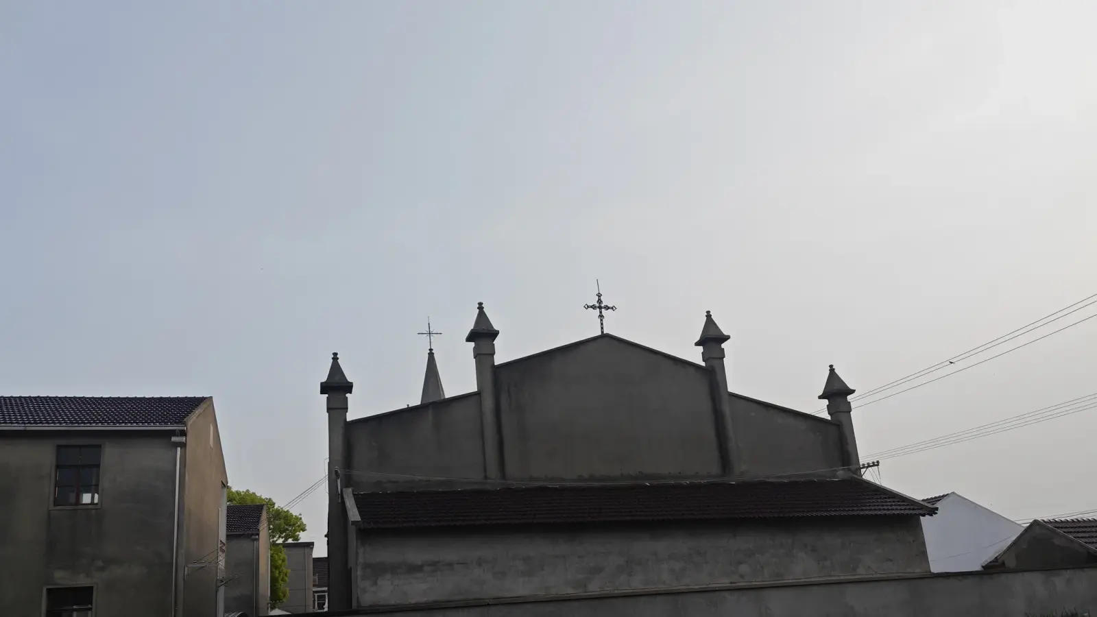 Dark gabled church front with a cross and four small pinnacles against a grey sky.