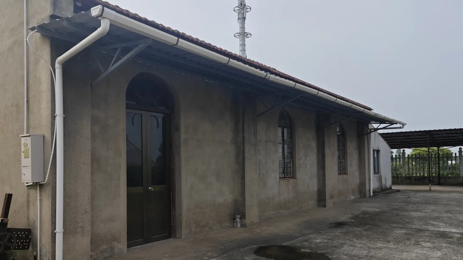 Side of a grey-rendered chapel with an arched wooden door, small arched windows and a tiled roof.