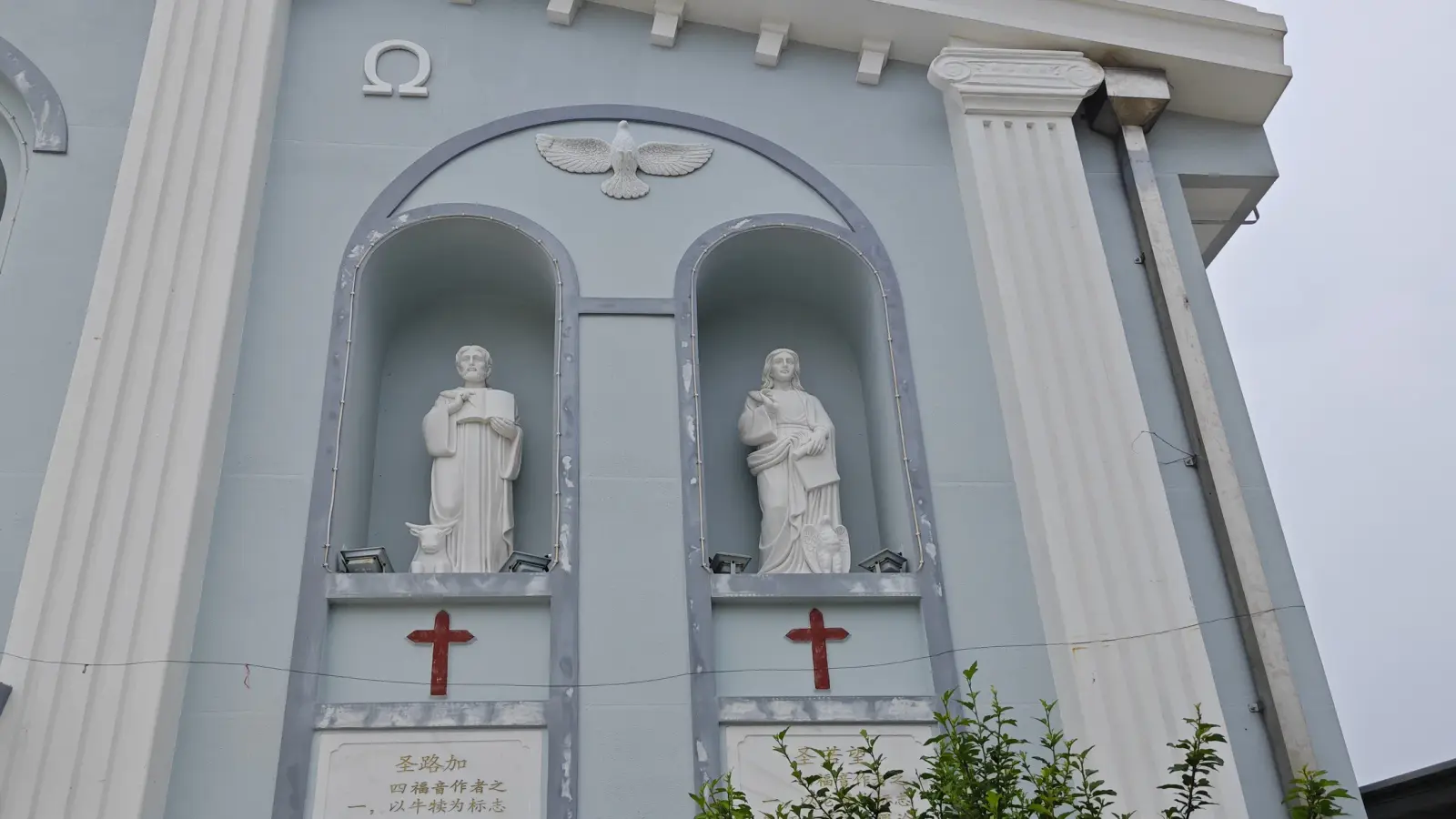 Two white statues in arched niches above red crosses and small inscription plaques.