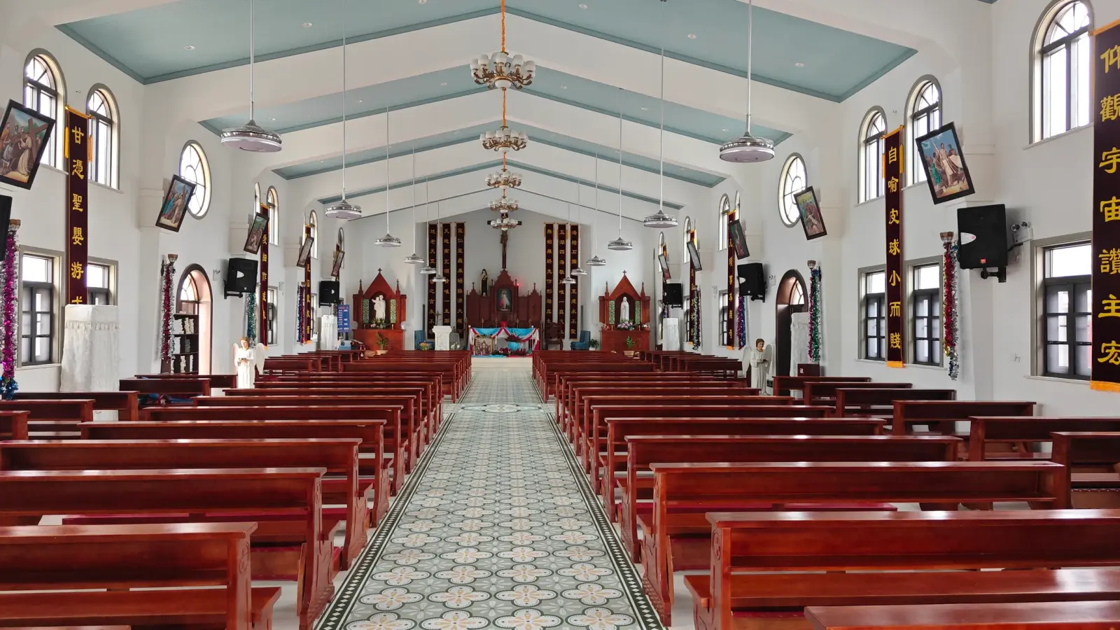 Church interior with red wooden pews, patterned tile aisle and a carved altar at the far end.