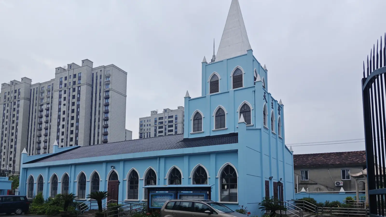 Side view of the blue church nave and tower, with tall apartment blocks in the background.